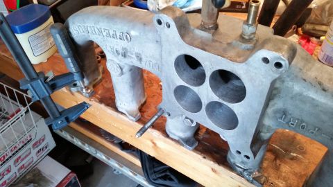 1981 Ford Bronco - An Offenhauser Dual Port intake manifold is clamped to a wooden surface on a workbench.