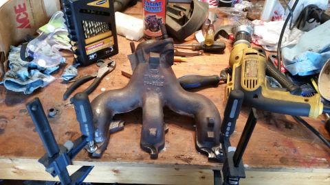 1981 Ford Bronco - Exhaust manifold and various tools laid out on a wooden workbench.