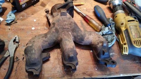 1981 Ford Bronco - A rusty Ford exhaust manifold is shown on a workbench with various tools, including pliers, screwdrivers, and a drill.