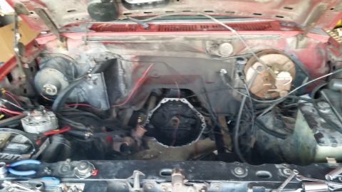 1981 Ford Bronco - The engine bay of a red vehicle shows the transmission bell housing and various engine components.