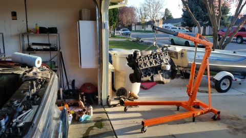 1981 Ford Bronco - An engine is suspended by an engine hoist, ready for removal or installation in a garage setting.