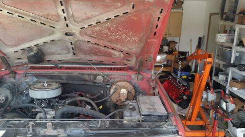 1981 Ford Bronco - The engine bay of a red vehicle is open, with an engine hoist and a red engine visible in the background.