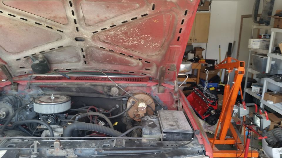 red vehicle engine bay, hood up, engine hoist with red engine nearby