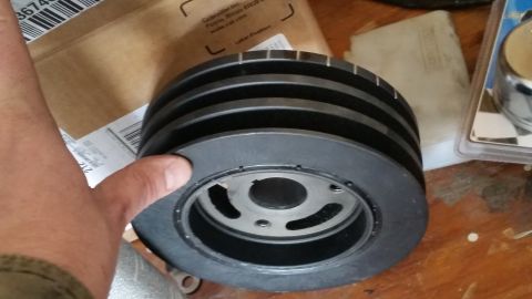 1981 Ford Bronco - A black multi-groove crankshaft pulley is shown, with a hand holding it against a backdrop of cardboard boxes and packaging.