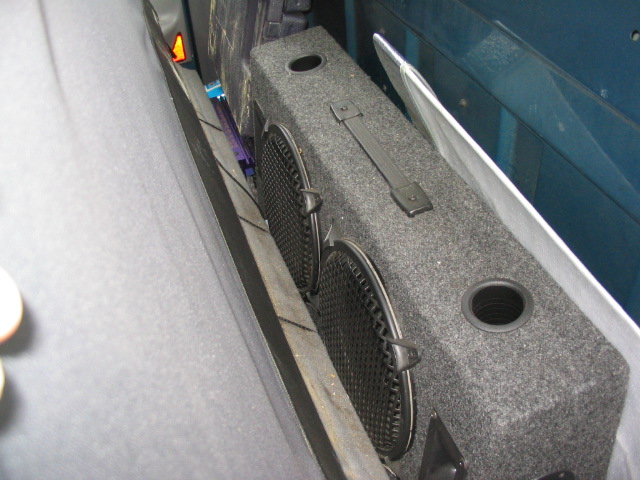Dual subwoofer box with two 10-inch speakers installed behind a vehicle seat