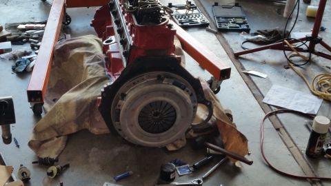 1981 Ford Bronco - Engine and transmission assembly resting on an engine hoist, surrounded by tools and shop clutter.