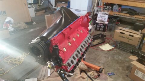 1981 Ford Bronco - A red V8 engine with black intake and valve covers is mounted on an orange engine stand in a garage.