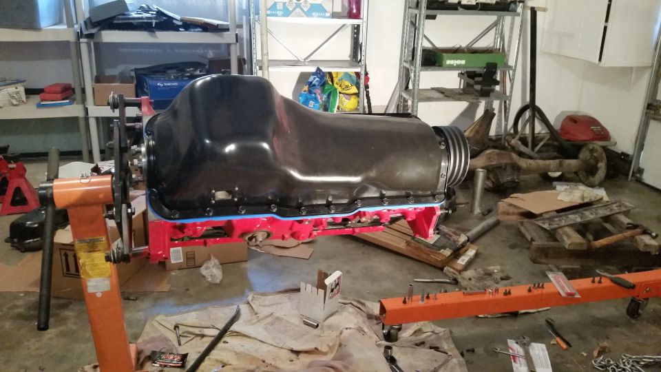 Engine block on an orange engine stand with parts scattered around a garage