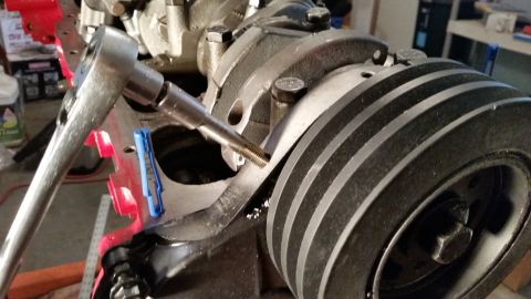 1981 Ford Bronco - Close-up of a socket wrench engaging a bolt on a multi-groove engine crankshaft pulley.