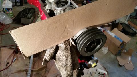 1981 Ford Bronco - A close-up view of a pulley and engine part, partially covered by cardboard, in a workshop setting.