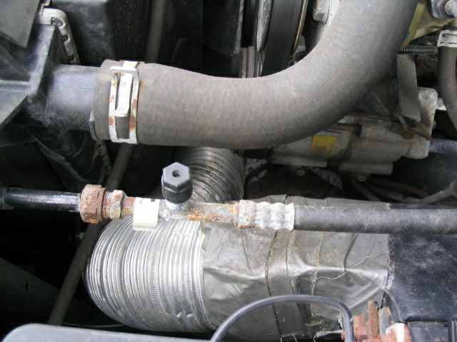 Close-up of engine bay hoses and metal ducting with visible rust on fittings