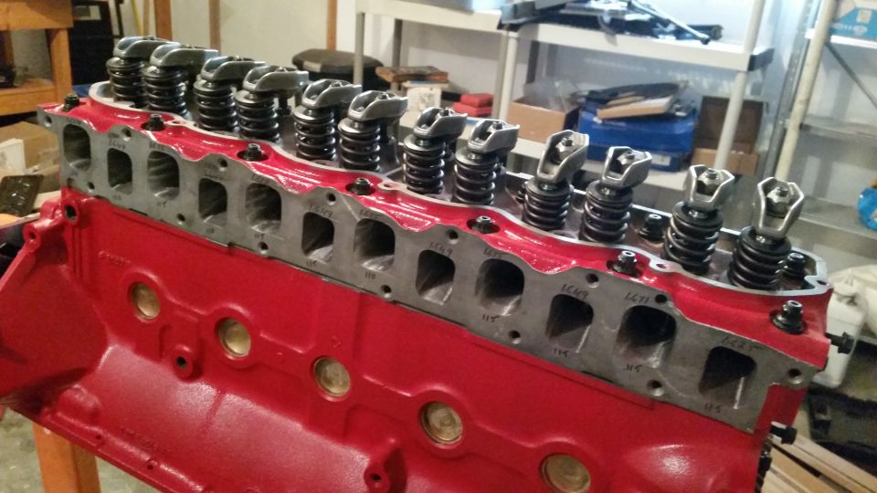 Red engine block with cylinder head and valve train components visible. Some casting numbers are visible on the head