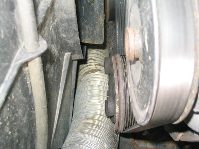 Close-up of a ribbed engine belt wrapped around pulleys, with a corrugated hose visible