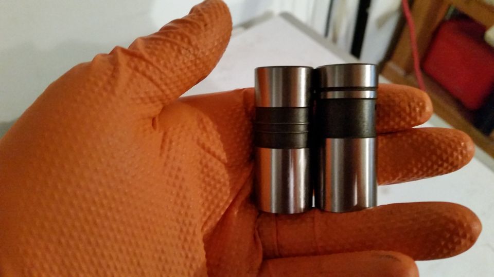 Two hydraulic valve lifters in an orange gloved hand