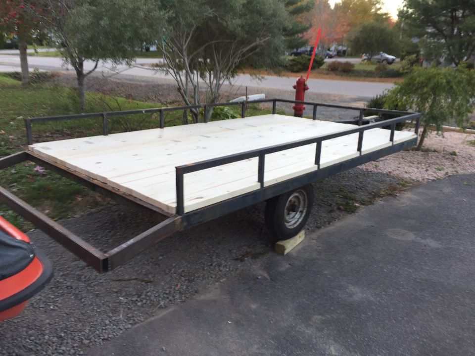 Side view of a wooden-decked utility trailer with metal railings