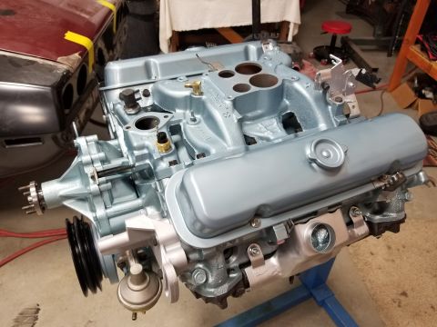 1969 Pontiac Firebird - A rebuilt V8 engine sits on a stand, with a portion of a red car body visible in the background.