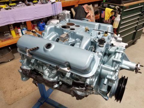 1969 Pontiac Firebird - A light blue V8 engine is mounted on a stand in a workshop setting, with various engine components visible.