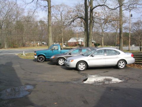 2004 Ford Taurus - A silver 2004 Ford Taurus sedan is parked next to a gray sedan and a blue pickup truck.