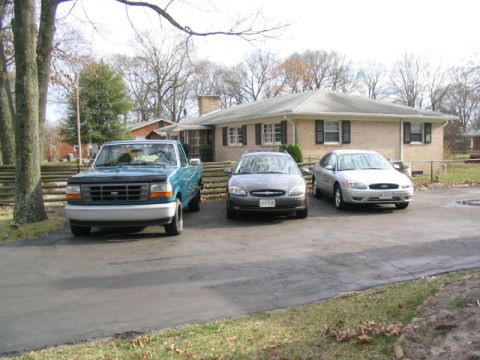 2004 Ford Taurus - Three vehicles are parked in a driveway in front of a residential house.