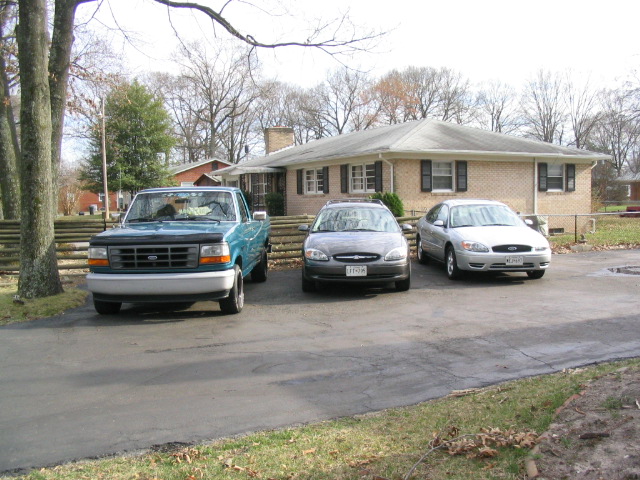 Blue Ford pickup truck, gray sedan, and silver sedan parked in front of a brick house