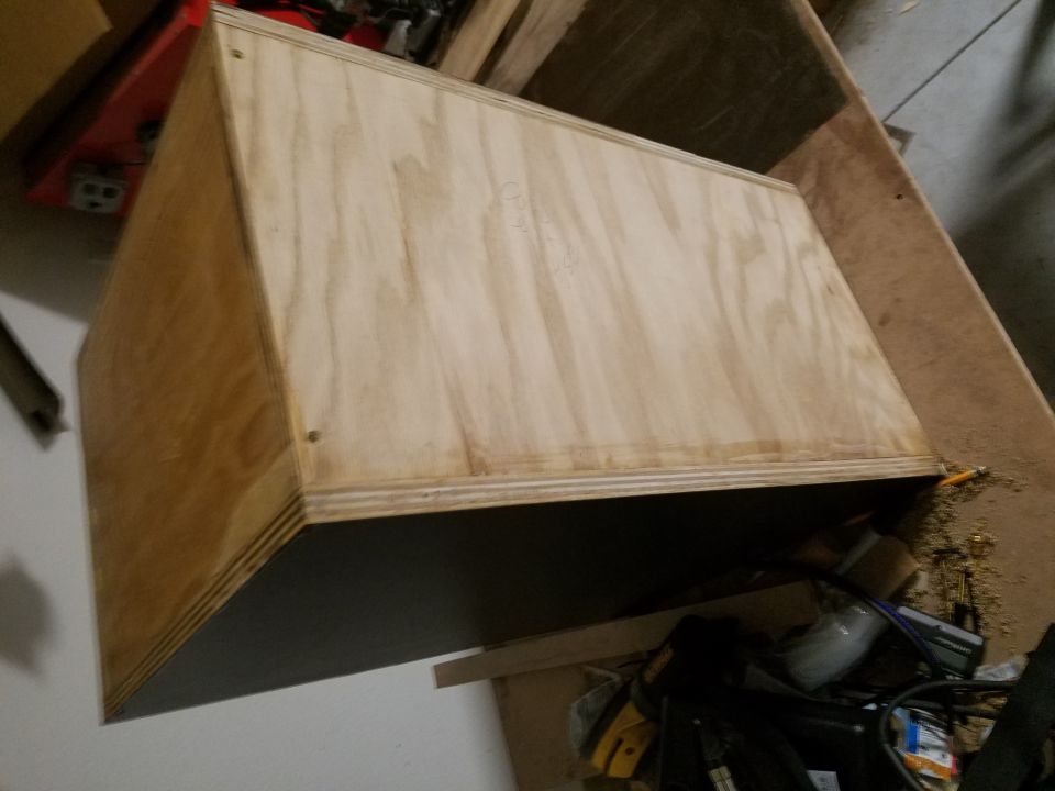 Photo of an unfinished plywood speaker box on a garage floor