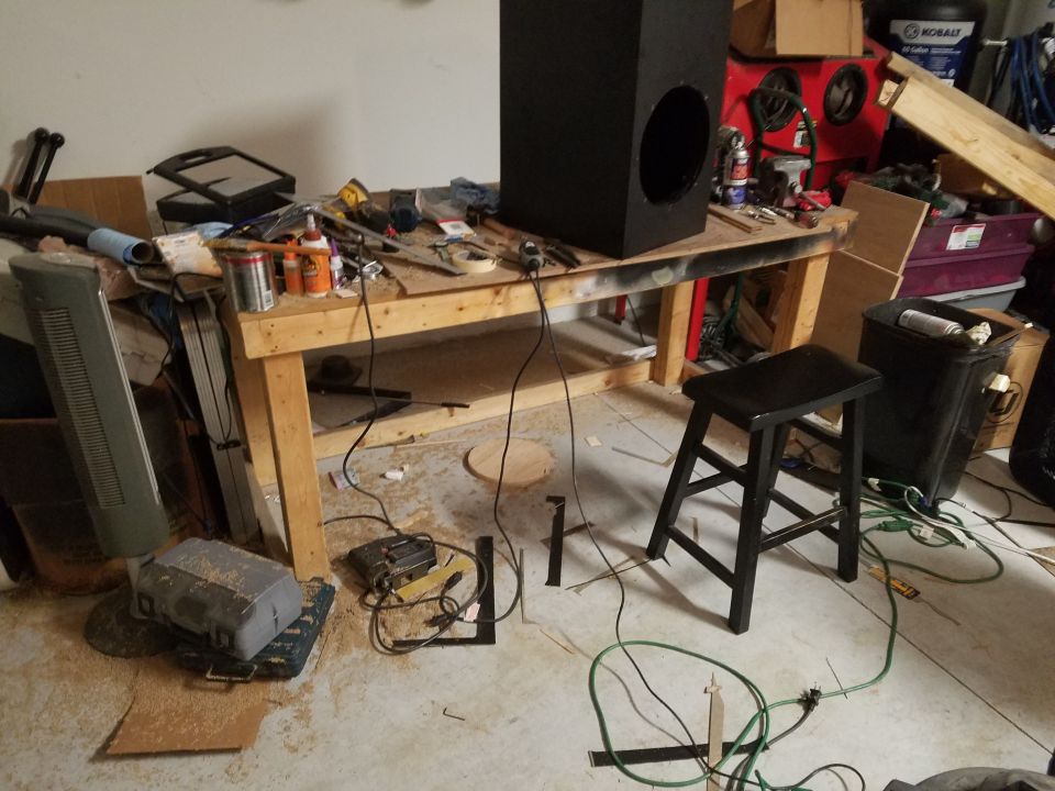 Photo of a cluttered garage workbench with tools and a speaker box