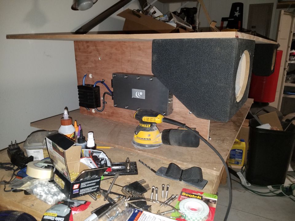 Subwoofer enclosure and amplifier mounted on plywood on a cluttered workbench