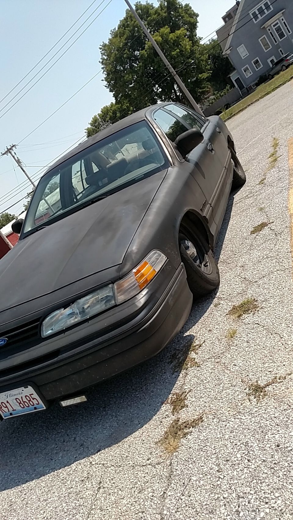 Matte black sedan parked in a gravel lot, front view.