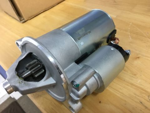 1996 Ford Bronco - A Motorcraft starter motor is shown on a wooden surface. The starter has a silver metal casing and a gear visible at the front.