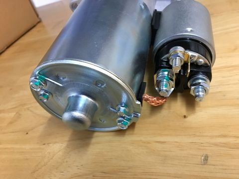 1996 Ford Bronco - A close-up view of two metal automotive starter motors with copper wiring and various bolts and nuts attached, resting on a wooden surface.