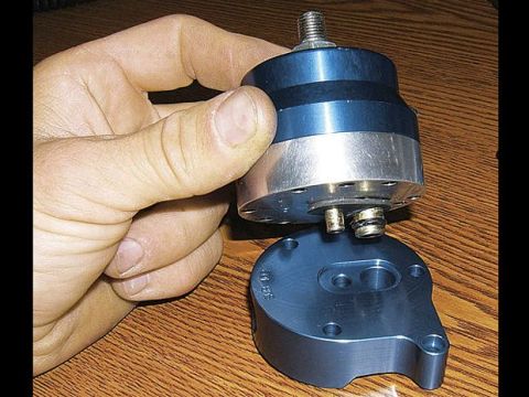 1996 Ford Bronco - A hand holds a blue and silver machined metal part with threaded studs above a matching blue base plate with two circular cutouts and mount…