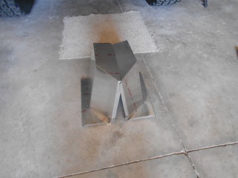 1992 Ford Bronco - Two unpainted metal components are riveted together and sit on a concrete floor next to a small rug. One component is a V-shape, and the ot…