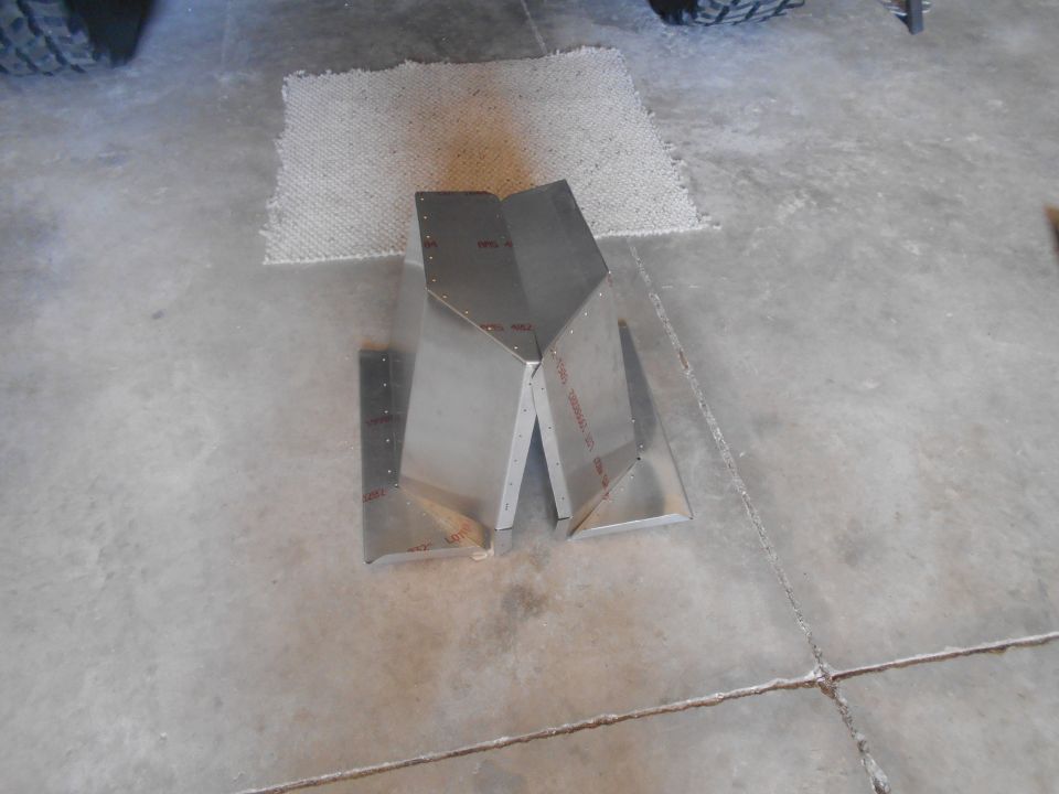 Two unpainted metal components riveted together on a concrete floor.