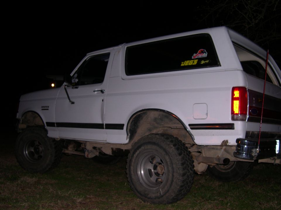 White lifted Ford Bronco on mud tires photographed from the rear at night