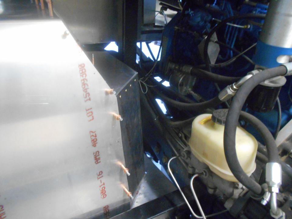 Shiny metal panel with text '6061-T6 AMS 4027 LOT 15499380' next to vehicle engine.