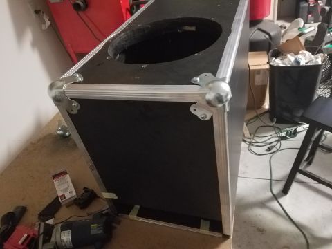 1994 Ford Bronco - A black speaker cabinet with metal reinforcement and a large circular opening sits on a concrete floor, surrounded by various items.