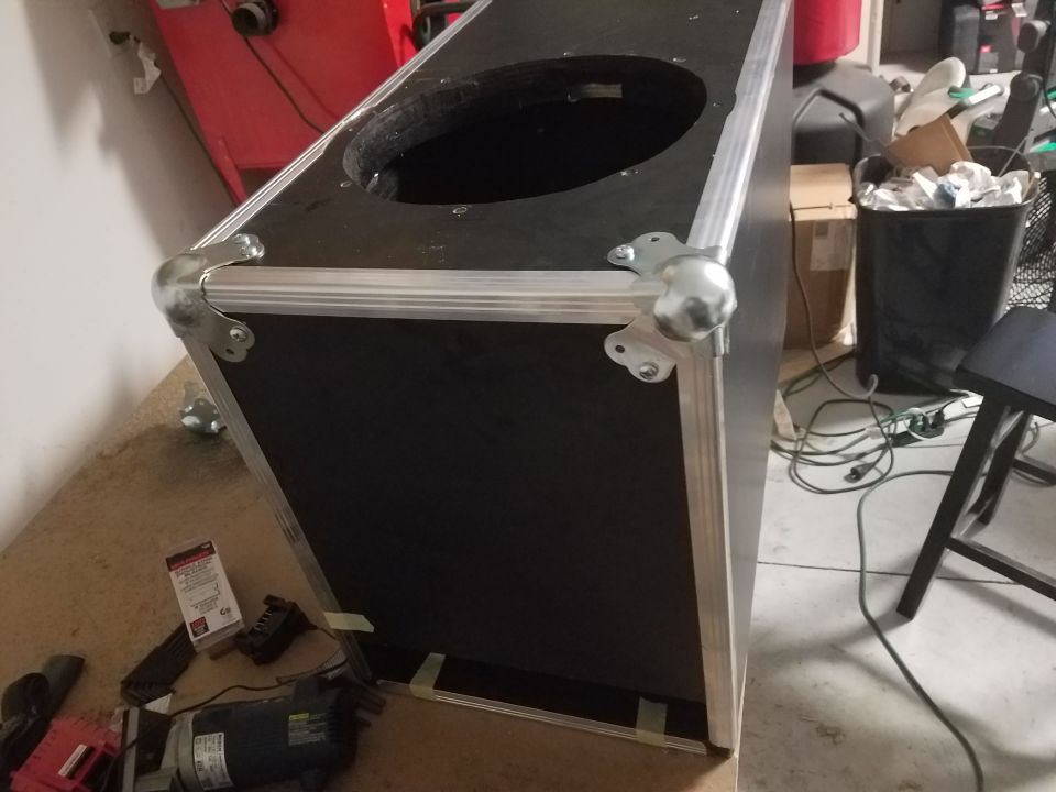 Speaker cabinet with metal corners and a circular opening on top, on a concrete floor