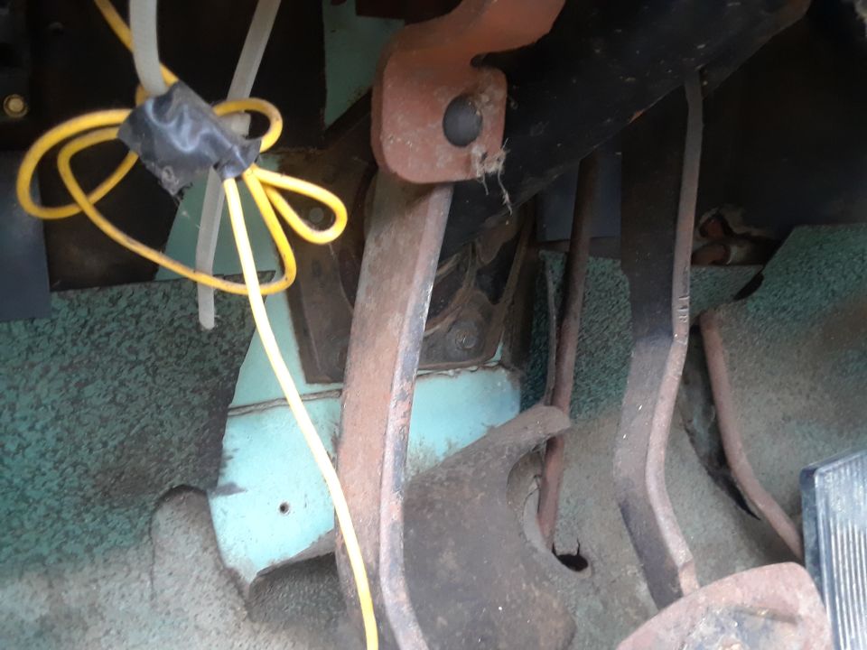 Close-up of vehicle floor pedals with yellow wire taped and zip-tied.
