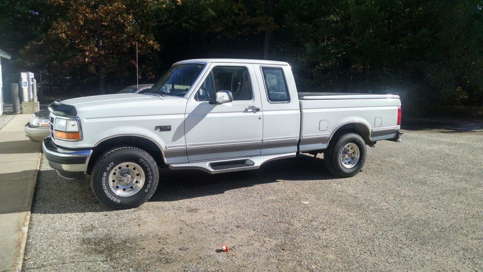 White 1990s Ford F-150 pickup truck, four-door, short bed, parked on gravel.