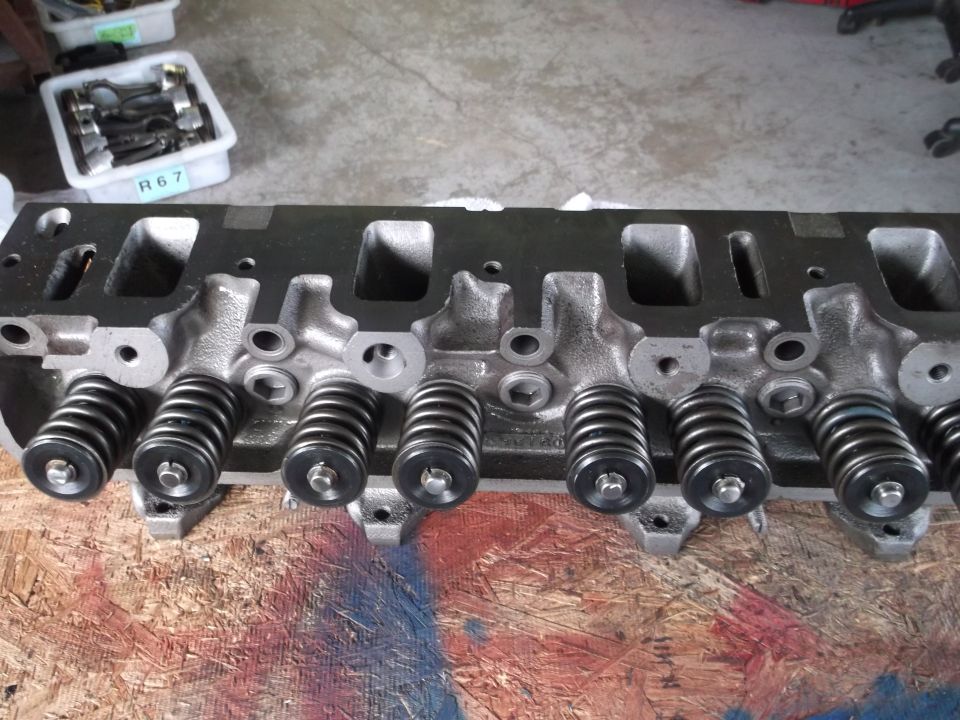 V8 engine cylinder head with valve springs and retainers, resting on painted wood.
