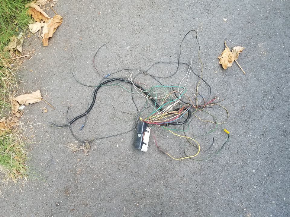 Tangled electrical wires and a black box on asphalt with dry leaves.