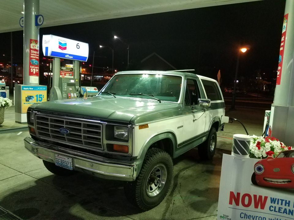1984 Ford Bronco at a Chevron gas station at night, fueling up.