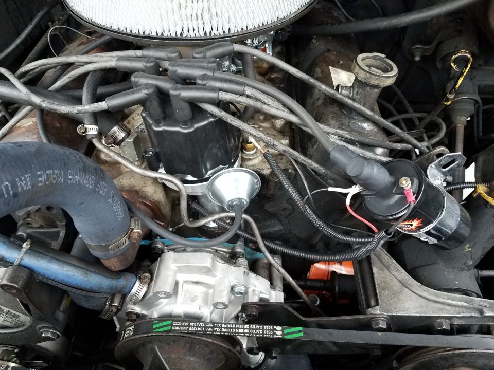 Close-up of a V8 engine bay with distributor, coil, hoses, and belts.