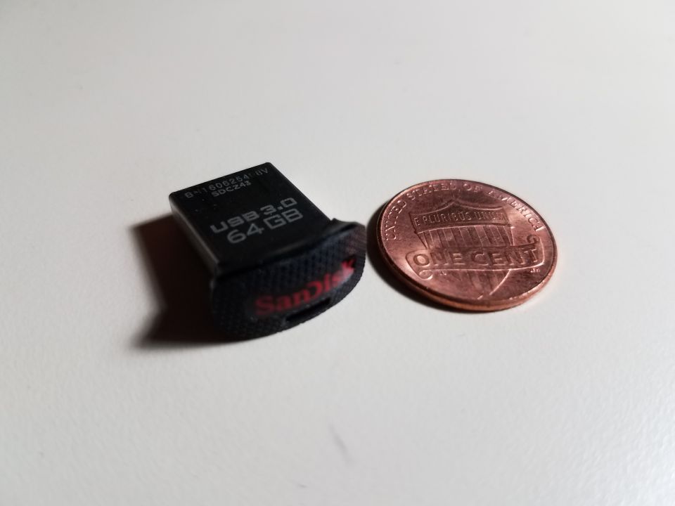 Black SanDisk USB 3.0 64GB flash drive next to a US penny.