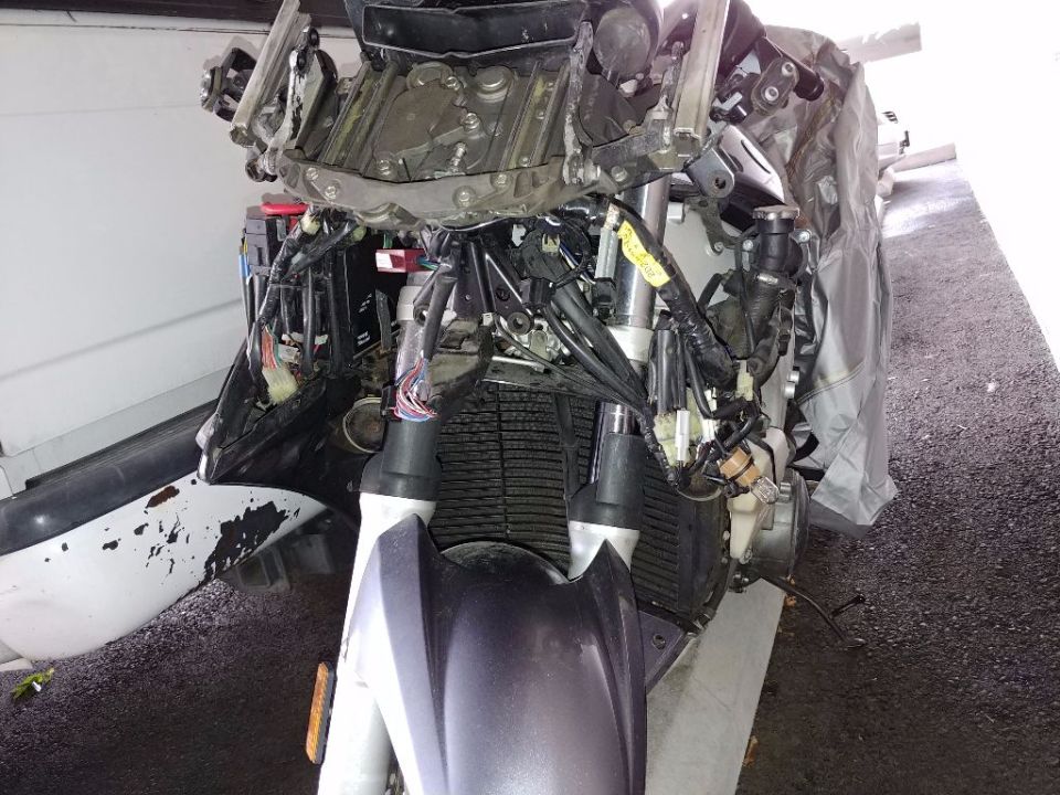 Damaged motorcycle front with exposed wiring and broken fairing.