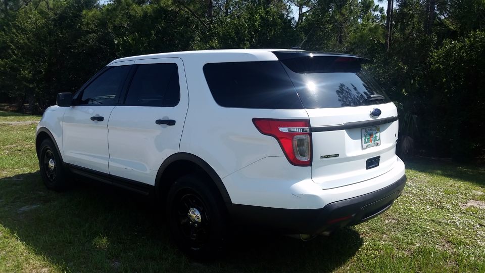 White 2013 Ford Explorer parked on grass with trees in background, rear passenger side view.