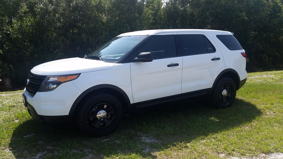 White 2013 Ford Explorer SUV parked on grass with trees in the background, side-front view.