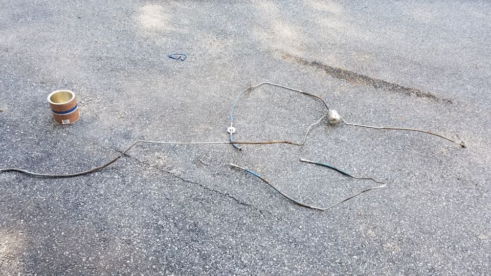 Metal tubing and a small cylinder on asphalt.