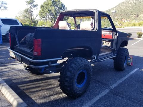 1995 Ford Bronco - The rear passenger side of a heavily modified, black Ford Bronco is shown parked in a lot. The vehicle features oversized off-road tires wi…