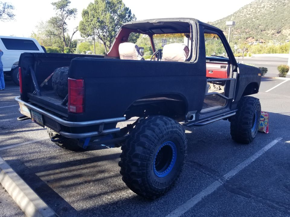 Modified black Ford Bronco with large off-road tires and blue rims, parked outdoors.